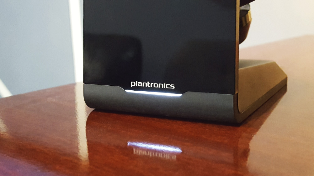 Plantronics Voyageri peakomplektide laadimise põhiandmed puidust laual, kaubamärgi logo all on valgustus
